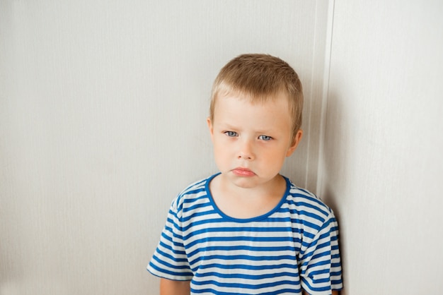 Portrait of a one sad little boy standing in the corner of the room, ready to cry