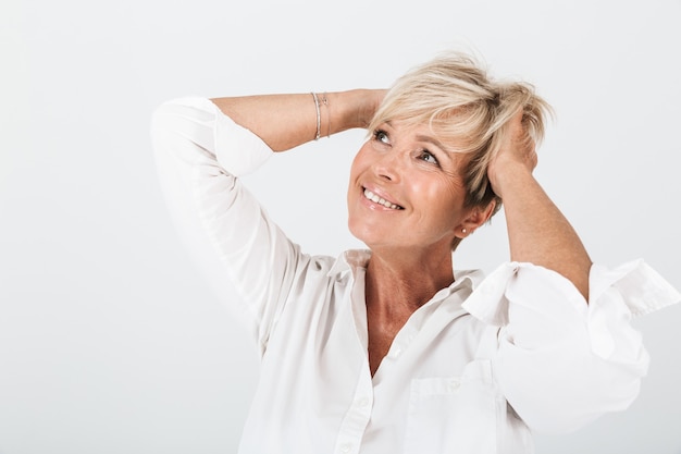 Portrait of optimistic adult woman with short blond hair grabbing her head and laughing at copyspace isolated over white wall in studio