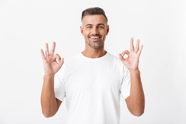 Portrait of optimistic man 30s with bristle wearing casual t-shirt showing ok sign isolated on white