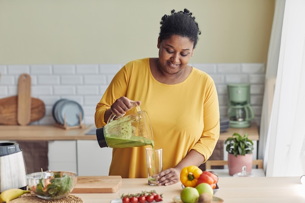 Portrait of overweight black woman enjoying healthy smoothie at home kitchen copy space