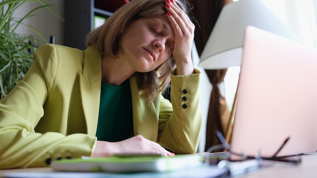 Photo portrait of overworked woman sitting in office and touching forehead with hand stressful and