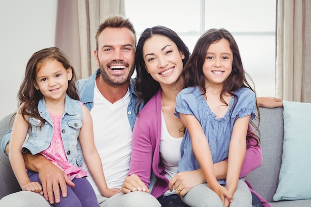 Portrait of parents sitting with daughters on sofa