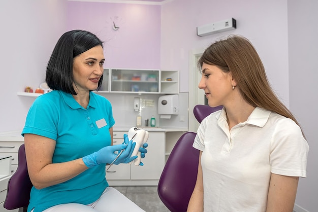 Portrait of patient with healthy teeth sitting in dental chair next to young female dentist