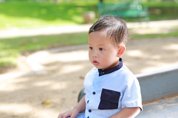 Портрет мирного азиатского ребёнка сидя на саде с смотреть вне.