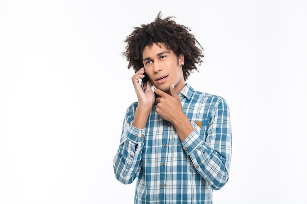 Portrait of a pensive afro american man talking on the phone isolated on a white wall