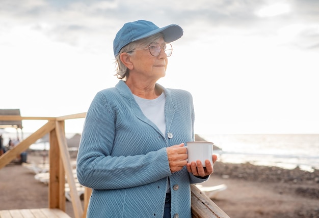 Portrait of pensive attractive senior woman in sea vacation standing at beach at sunset