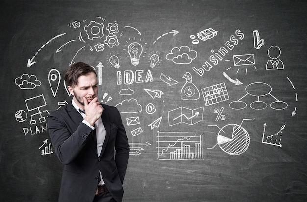 Portrait of a pensive bearded businessman standing near a blackboard with business idea drawing on it. Concept of launching a new business project.