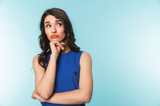 Portrait of a pensive beautiful young brunette woman standing over blue