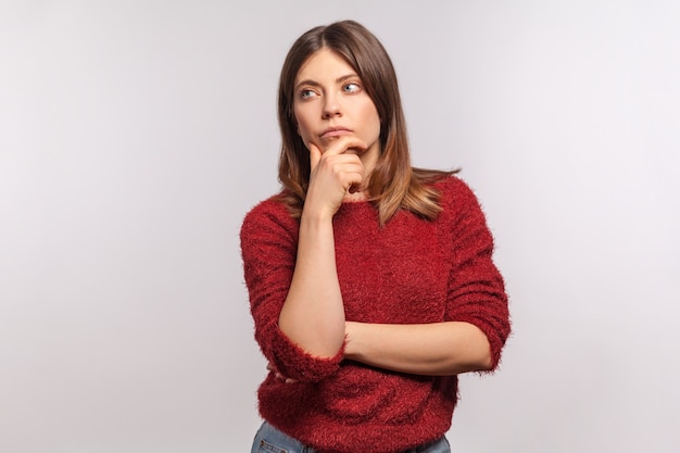 Portrait of pensive girl in shaggy sweater holding chin having doubt and suspicion feeling