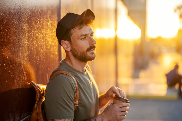 Portrait of a pensive man leaning on the wall on the street and taking a break with cup of coffee