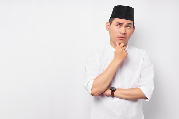 Portrait of pensive young Asian Muslim man looking at empty space touching his chin thinking about offer isolated on white background People religious Islamic lifestyle concept