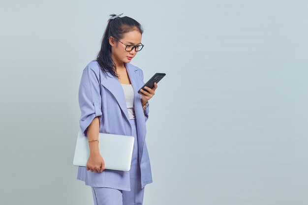 Portrait of pensive young Asian woman holding laptop and using mobile phone, reading news message isolated on white background