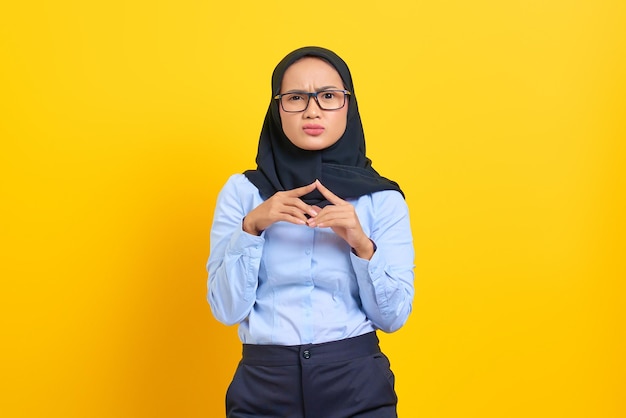 Portrait of pensive young Asian woman looking seriously thinking about a question isolated on yellow background