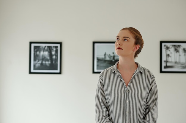 Portrait of pensive young woman standing in art gallery enjoying beauty of photos