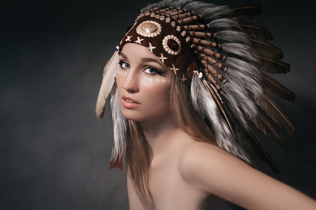 회색 배경의 연기 속에서 아메리칸 인디언 복장을 한 완벽한 여성 초상화. 깃털로 만든 모자. 신비한 신비한 사람, 섹시한 몸매, 아름다운 얼굴