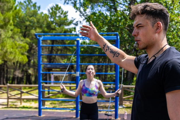 Portrait of a personal trainer with a whistle giving the order to start the exercise while in the background is a girl skipping rope Physical training