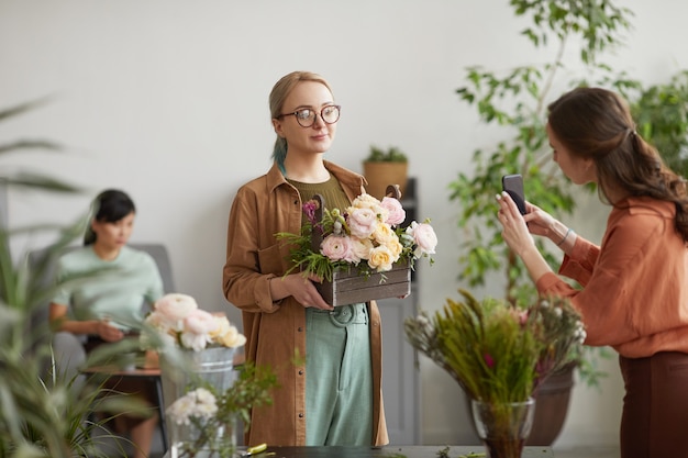 portrait pf smiling female florist holding floral composition while posing for photo in flower shop, copy space