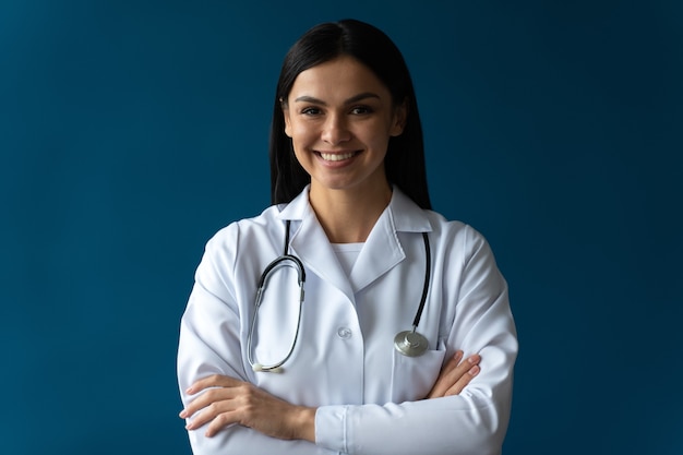 Foto ritratto di un medico di famiglia attraente e amichevole che indossa un camice bianco da laboratorio e uno stetoscopio sorridente amichevole e in posa con le braccia incrociate sullo sfondo di colore blu isolato