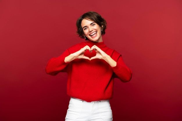 Portrait photo of joyful attractive woman making a heart gesture with her hands