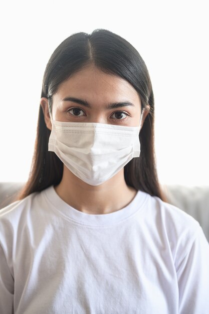 Foto foto del ritratto di giovane donna asiatica che indossa la maschera chirurgica in casa per proteggere il coronavirus (covid-19) durante la crisi di pandemia di epidemia di virus in tutto il mondo.