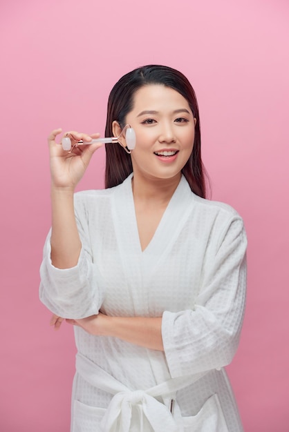 Portrait photo of a young woman looking relaxed use while using a natural white quartz face roller.