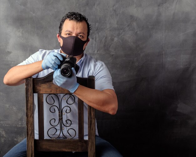 Portrait photographer in his studio sitting down on a chair wearing surgical gloves and a face mask