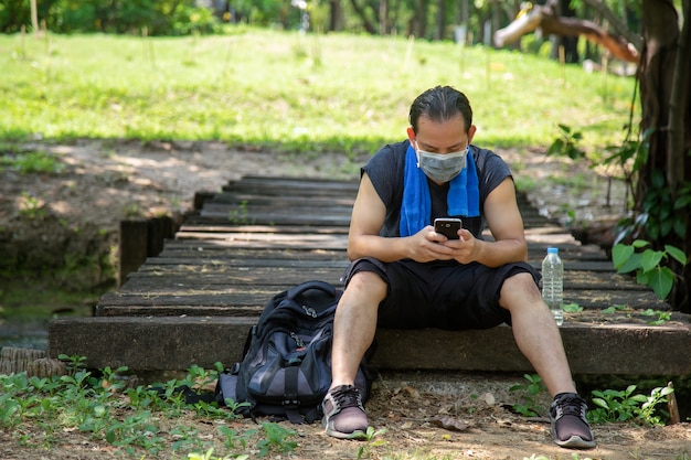 Portrait picture an Asian man in black sportswear wearing a face mask sitting on a wooden plank