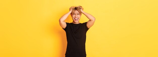 Photo portrait of pissedoff angry asian man tossing haircut and yelling furious standing over yellow backg