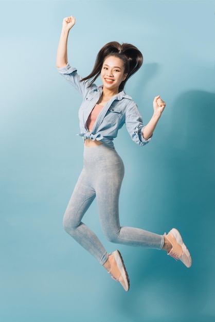 Portrait of playful crazy girl jumping in the air looking at camera enjoying weekend having perfect mood on light blue background