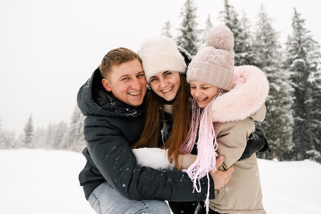 Portrait of playful happy family in winter forest. Mother, father and dauther playing with snow. Enjoying spending time together. Family concept