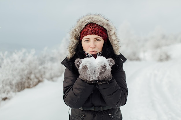 山に立っている間に手から雪を吹く遊び心のある女性の肖像画