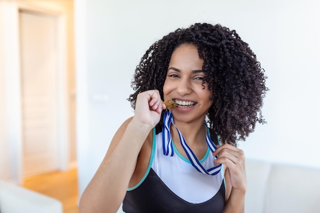 脇に笑みを浮かべて彼女の金メダルを噛む遊び心のある若い女性ランナーの肖像スポーツアクティブなライフスタイルの動機付けの概念