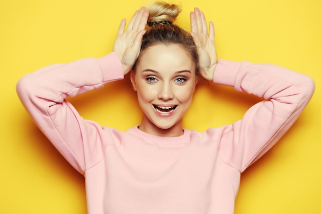 Portrait of playful young pretty blond woman showing horns and making faces Isolated on yellow background