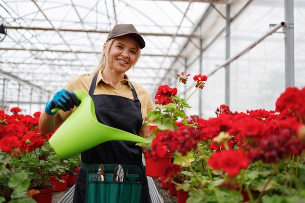 温室で灌<unk>箱から花瓶に植えられた植物に水を注ぐ愉快な女性花屋の肖像画