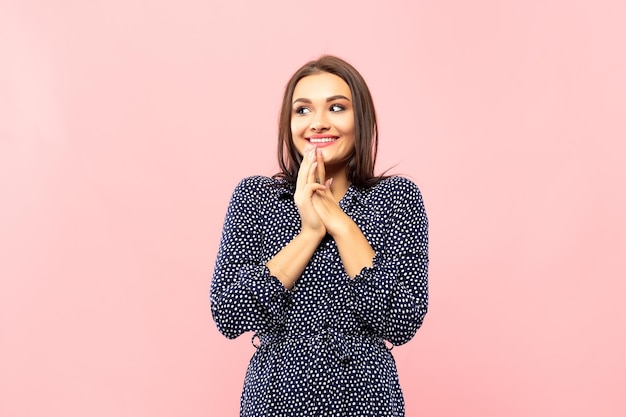 Portrait of pleasant looking young woman with toothy smile keeps hands near cheek dressed in blue