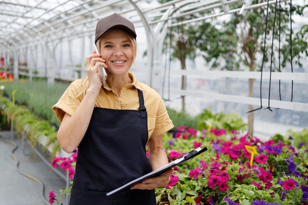 Ritratto di una piacevole donna di mezza età che parla al telefono in una serra di fiori