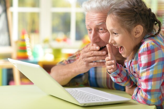 Portrait of pleasantly surprised grandfather and granddaughter with laptop