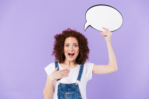 Portrait of pleased redhead curly woman 20s smiling while holding blank thought bubble