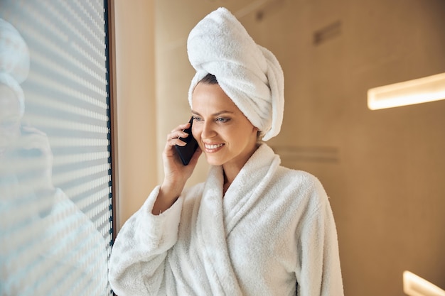 Portrait of a pleased woman with a bath towel on her head calling on the phone