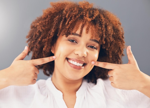 Portrait point and teeth with black woman smile or oral hygiene against grey studio background Face African American female or lady with gesture for mouth happiness or dental health for wellness