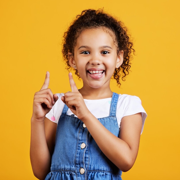Portrait pointing up and girl with smile branding development and happiness against a studio background face female child and young person gesture for space direction and showing with choice