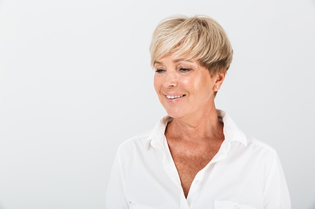 Portrait of positive adult woman with short blond hair smiling at camera isolated over white wall in studio