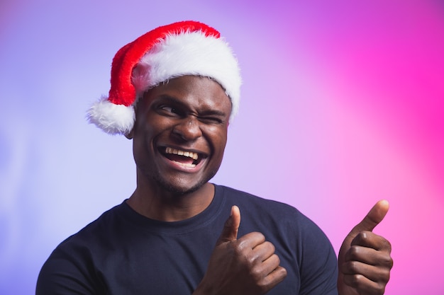 Портрет позитивного афро-американского улыбающегося человека в новогодней шапке и повседневной футболке на красочных