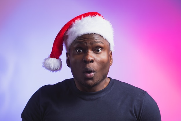 Portrait of positive african american smiling man in santa hat and casual tshirt on colourful