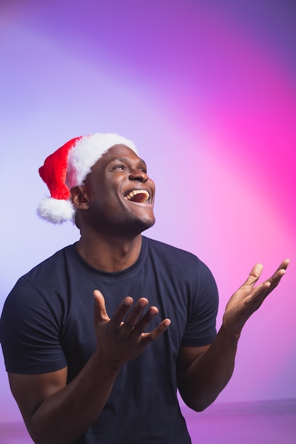 Portrait of positive african american smiling man in santa hat and casual tshirt on colourful