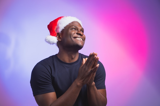 Portrait of positive african american smiling man in santa hat and casual tshirt on colourful