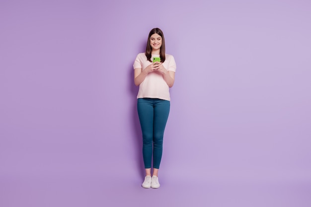 Portrait of positive beautiful lovely lady hold smartphone typing look screen on purple background