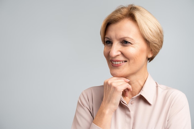 Ritratto di donna bionda positiva in piedi, distogliendo lo sguardo con un sorriso gioioso e affascinante, godendosi la vita. colpo dello studio dell'interno isolato su fondo grigio