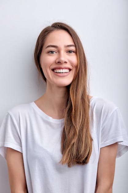 Portrait of positive caucasian woman smiling at camera having perfect toothy smile wearing white cas...