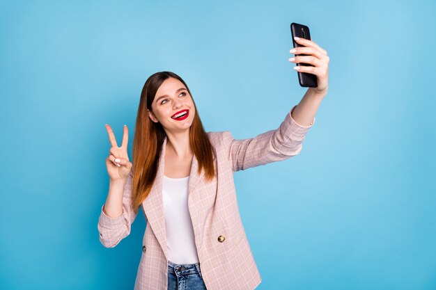 Portrait of positive cheerful blogger girl make selfie smartphone vsign